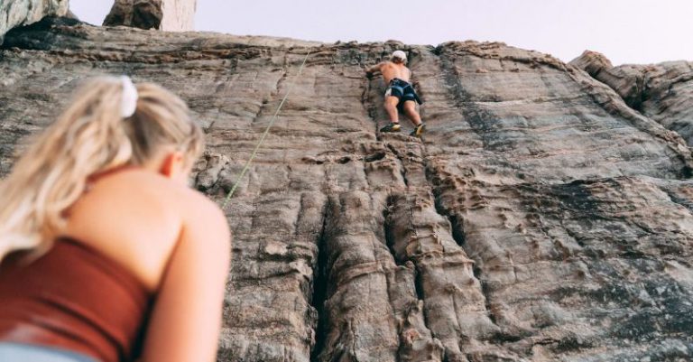 Bravery Cliff - Woman and Man Climbing Up a Rocky Wall