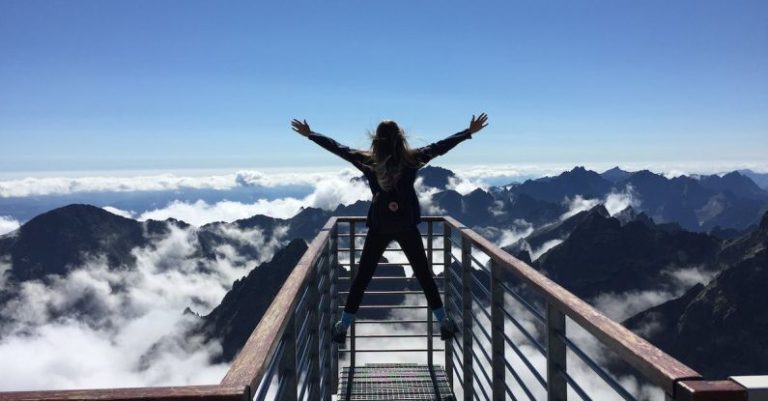 Woman Mountain - Person Standing on Hand Rails With Arms Wide Open Facing the Mountains and Clouds