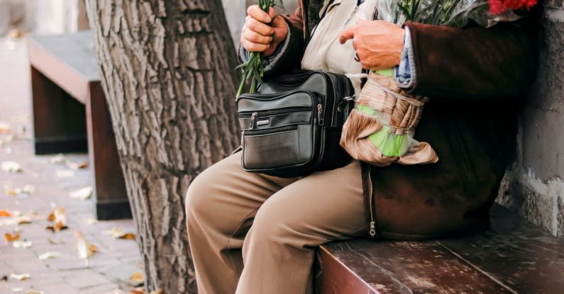 Shield Roses - An old man sitting on a bench holding a bunch of red roses