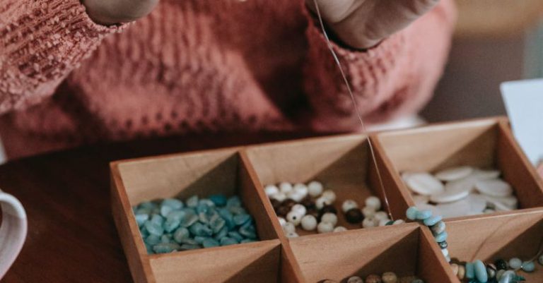 Workspace Harmony - Crop unrecognizable ethnic female in light orange sweater doing beading with colorful beads and fishing line