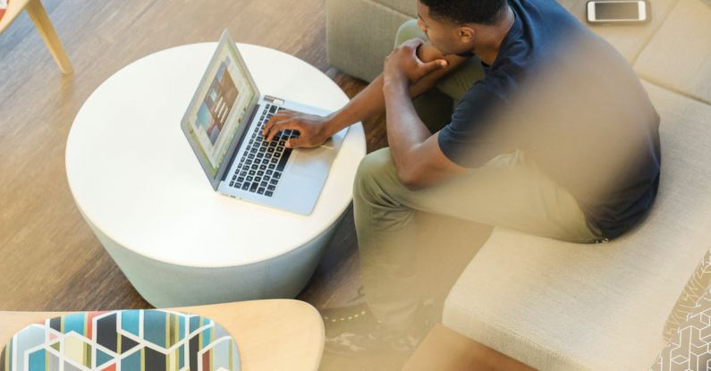 Laptop Home - Man Using Gray Laptop While Sitting on Beige Sofa