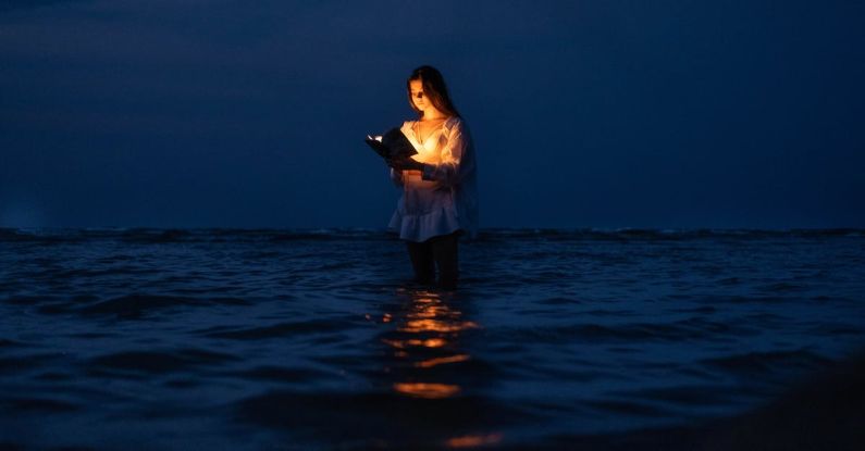 Books Horizon - A Woman Standing in the Water with a Book Illuminating Her Face