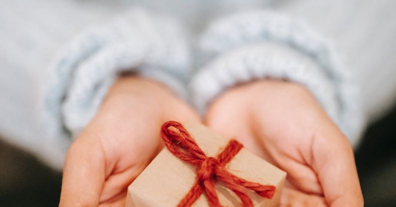 Hand Gift - High angle crop unrecognizable female in blue sweater demonstrating small wrapped present box on hands